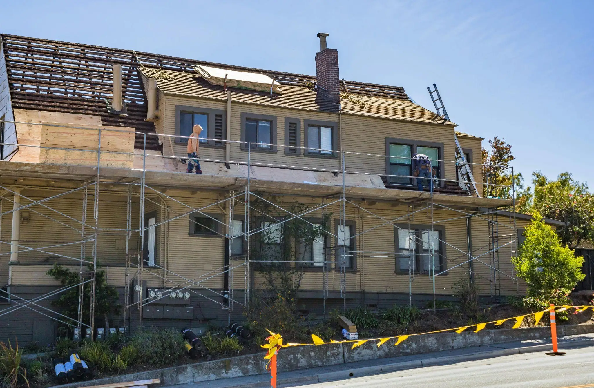 Workers on scaffolding renovating roof of two-story house on sunny day