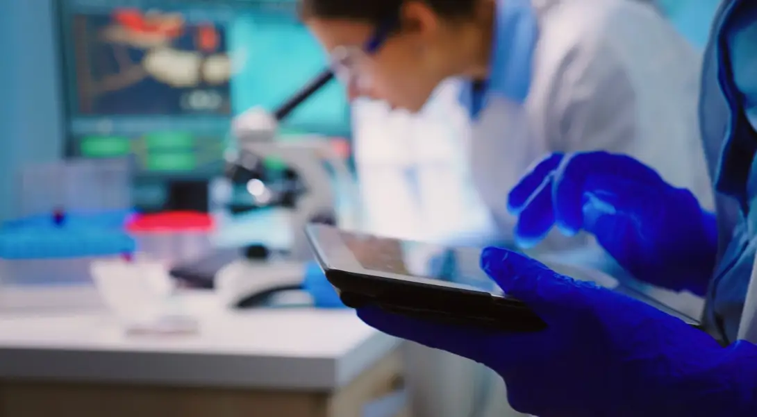 Researcher using digital tablet in a laboratory with microscope and scientific charts in background