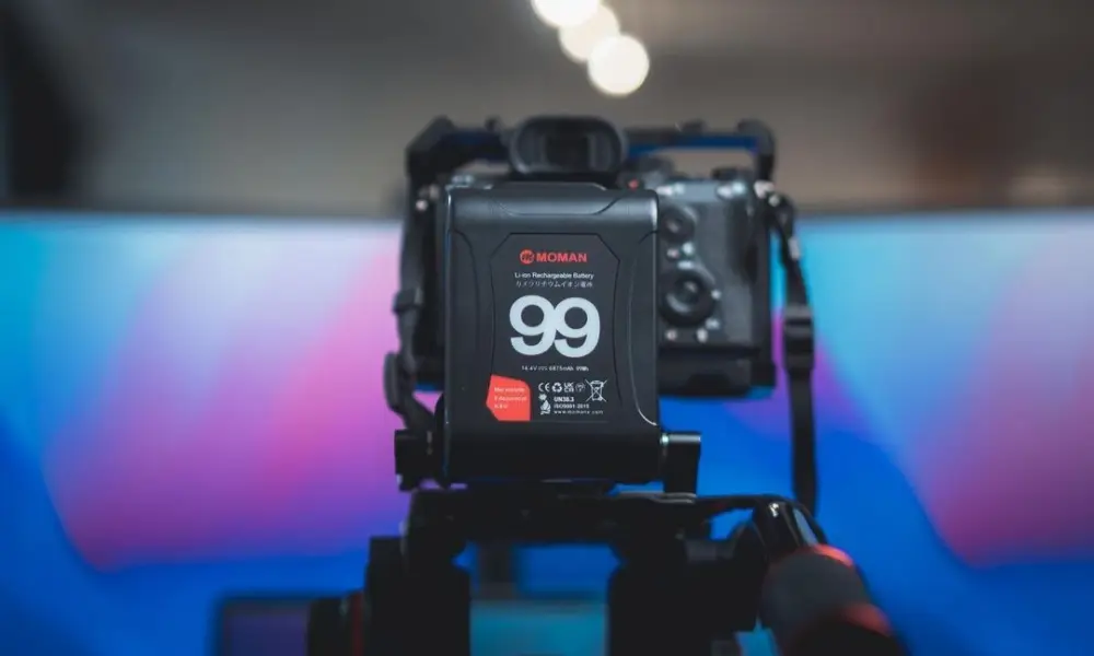 Camera with attached rechargeable battery on tripod against colorful blurred background