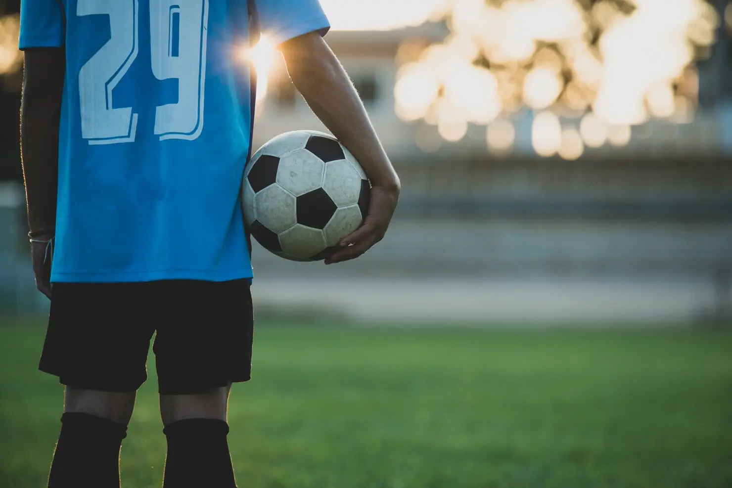 Soccer player holding ball on grassy field during sunset