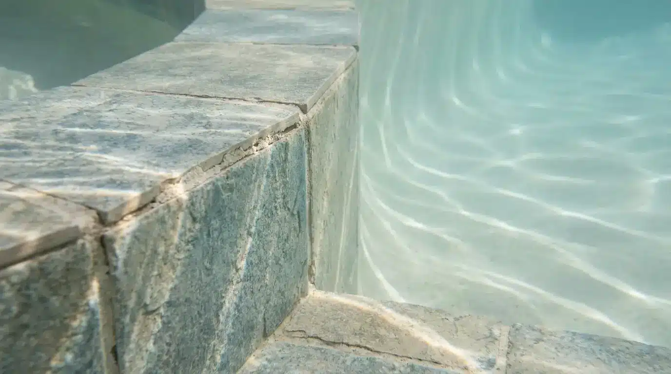 Pool edge with textured stone tiles and clear blue water reflections