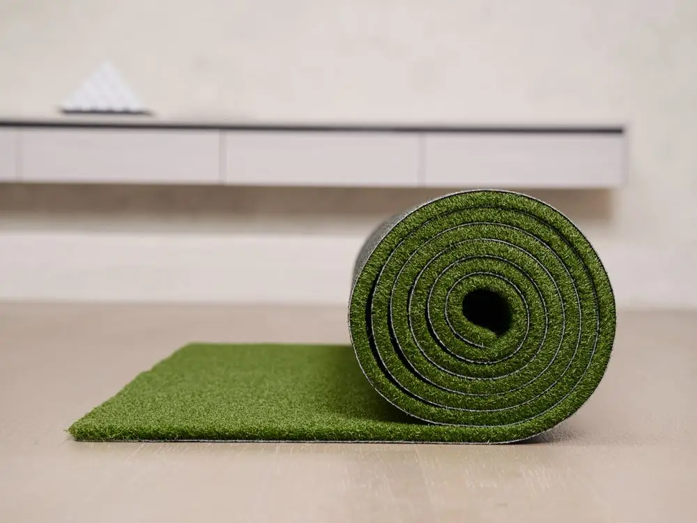 Rolled artificial grass mat on light wood floor in modern room