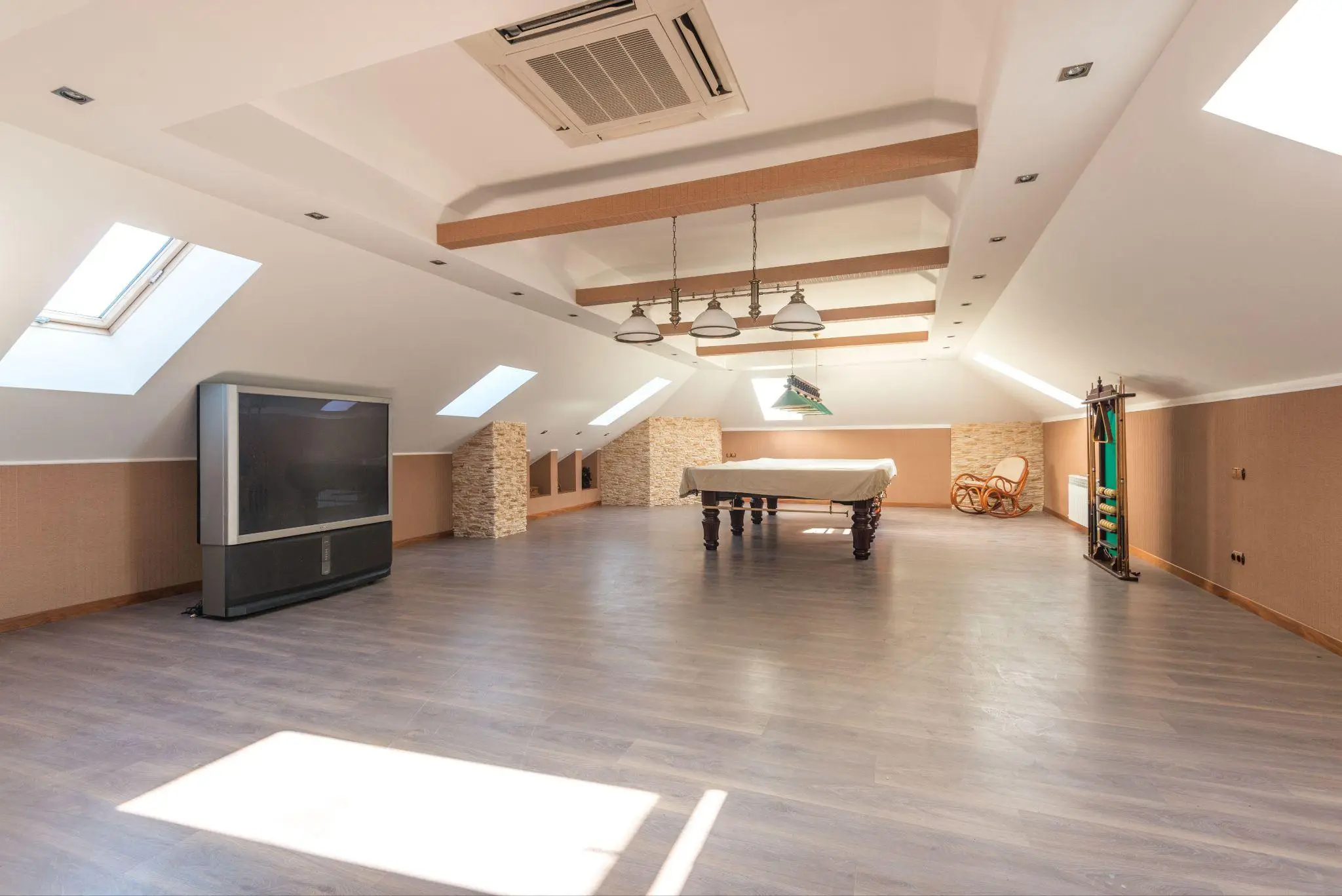Spacious attic game room with billiard table, large TV, and skylights under bright daylight