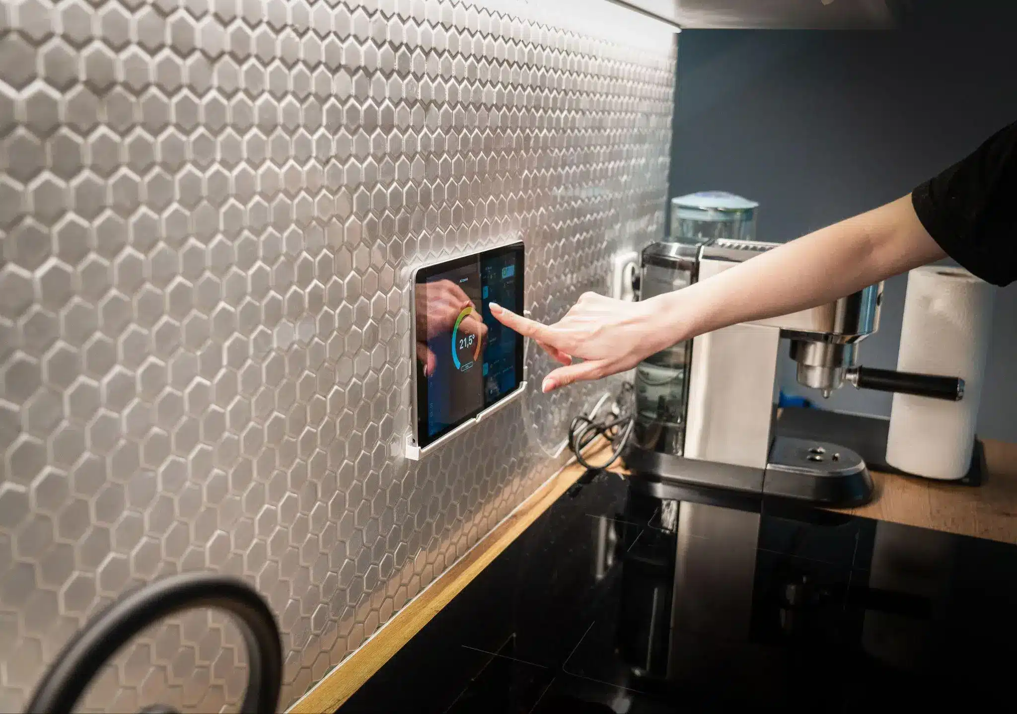 Hand adjusting smart home control panel on hexagonal tiled kitchen wall