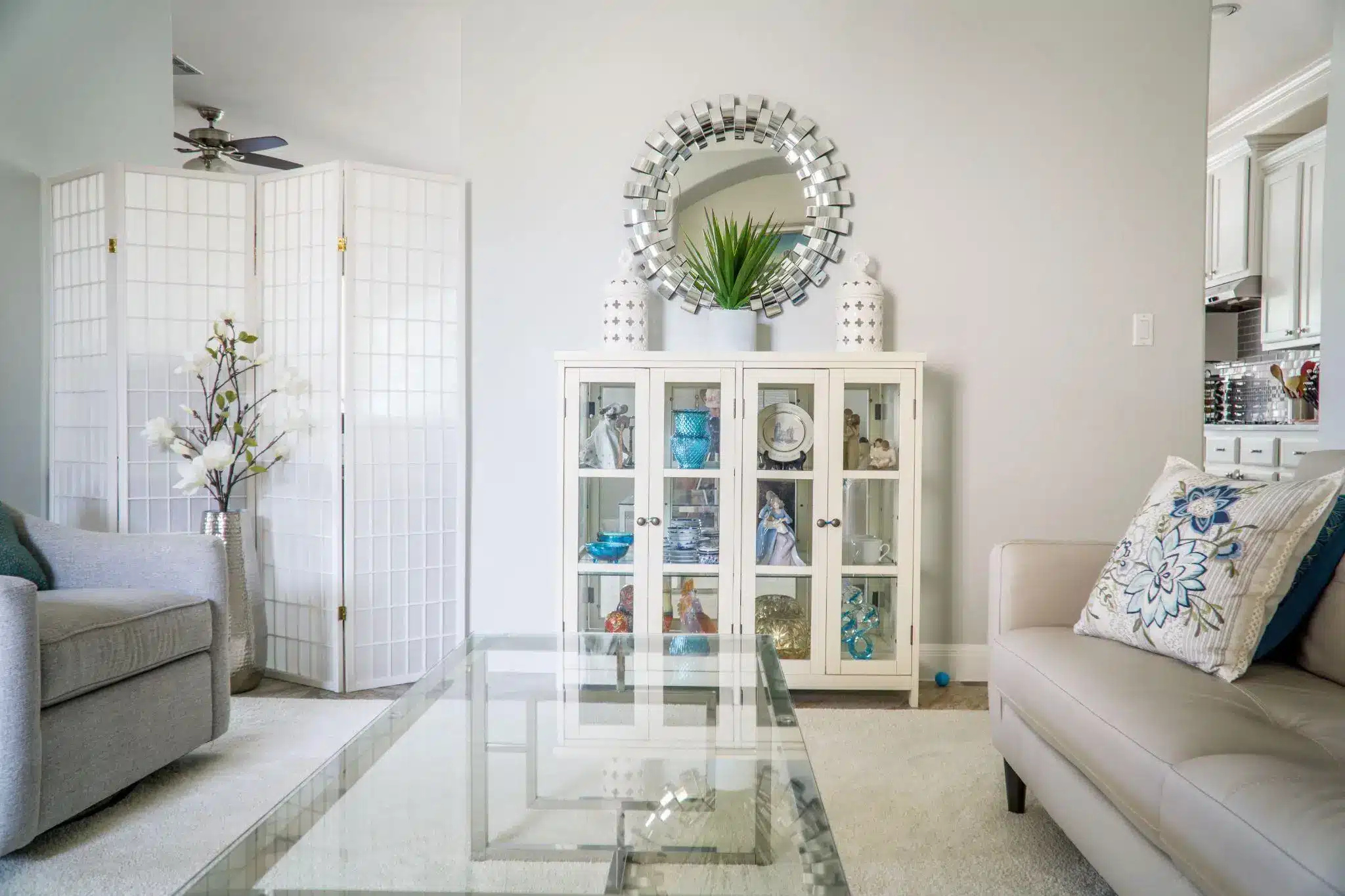 Glass coffee table in modern living room with decorative cabinet and floral cushions on sofa
