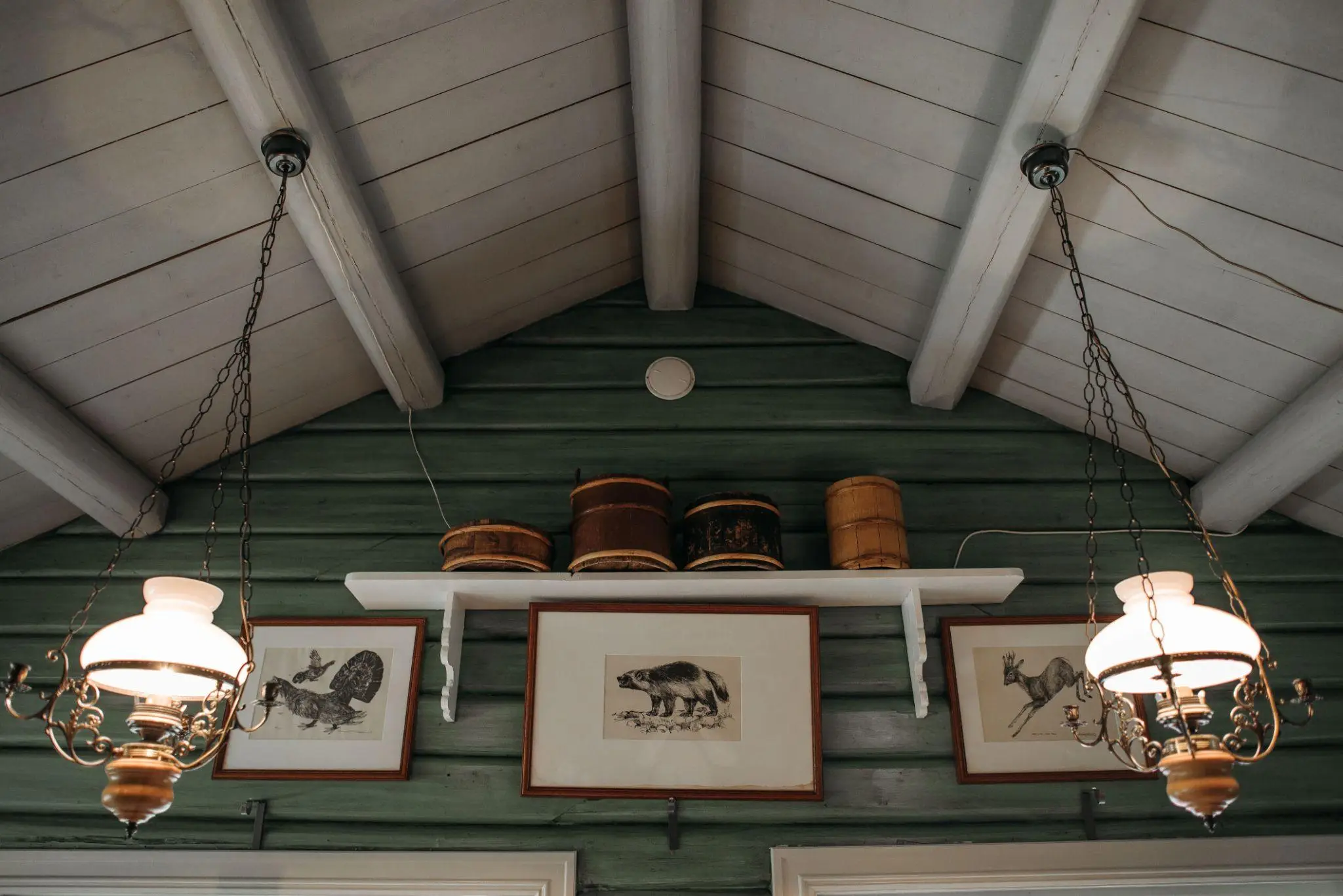 Vintage chandeliers and framed wildlife prints on green wood wall with vaulted ceiling