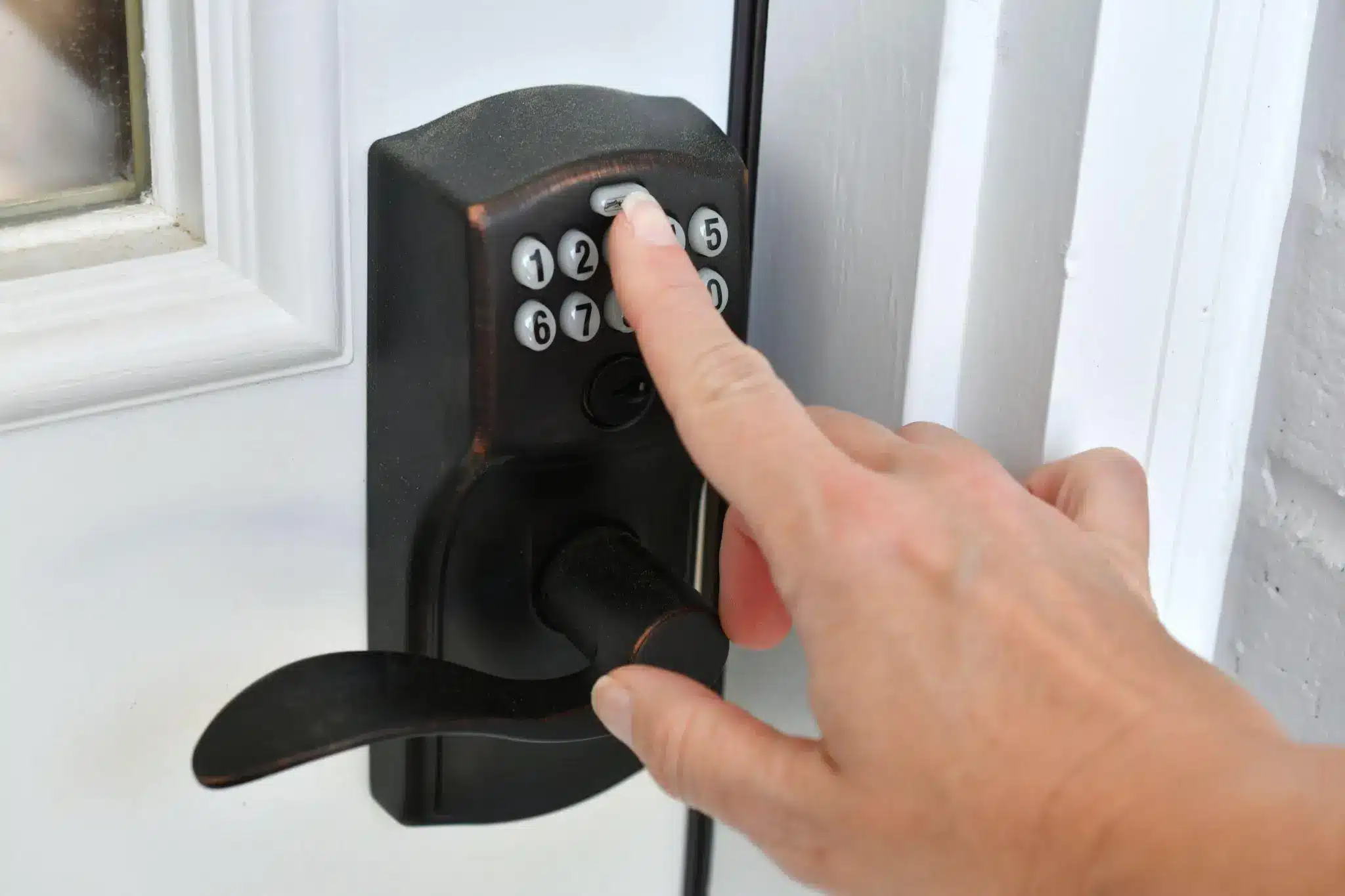 Hand entering code on black keypad door lock in close-up view