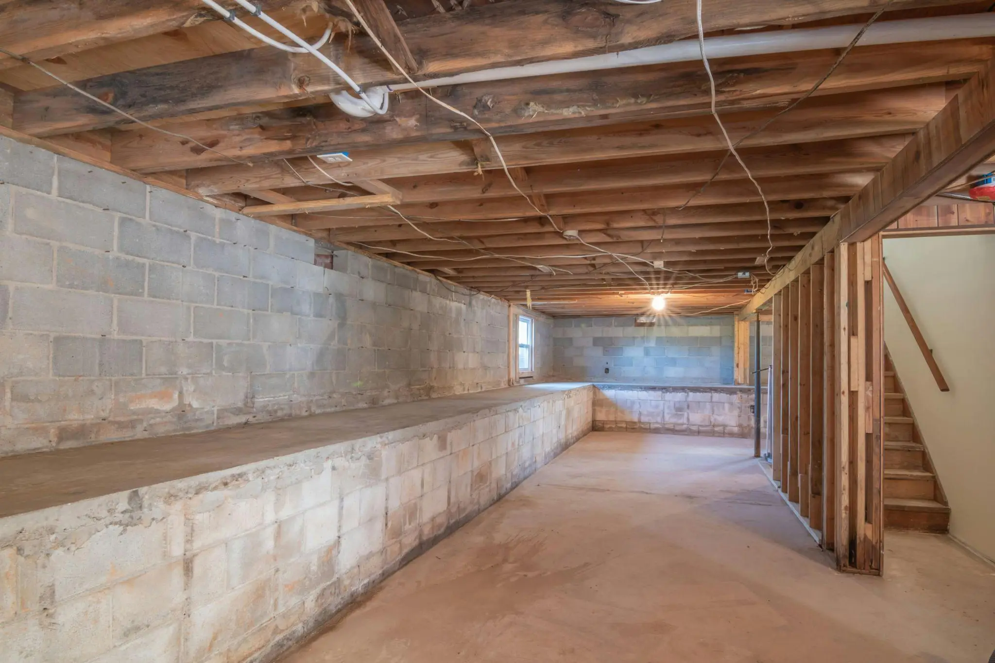Unfinished basement with exposed wooden beams and cinder block walls, lit by a single bulb