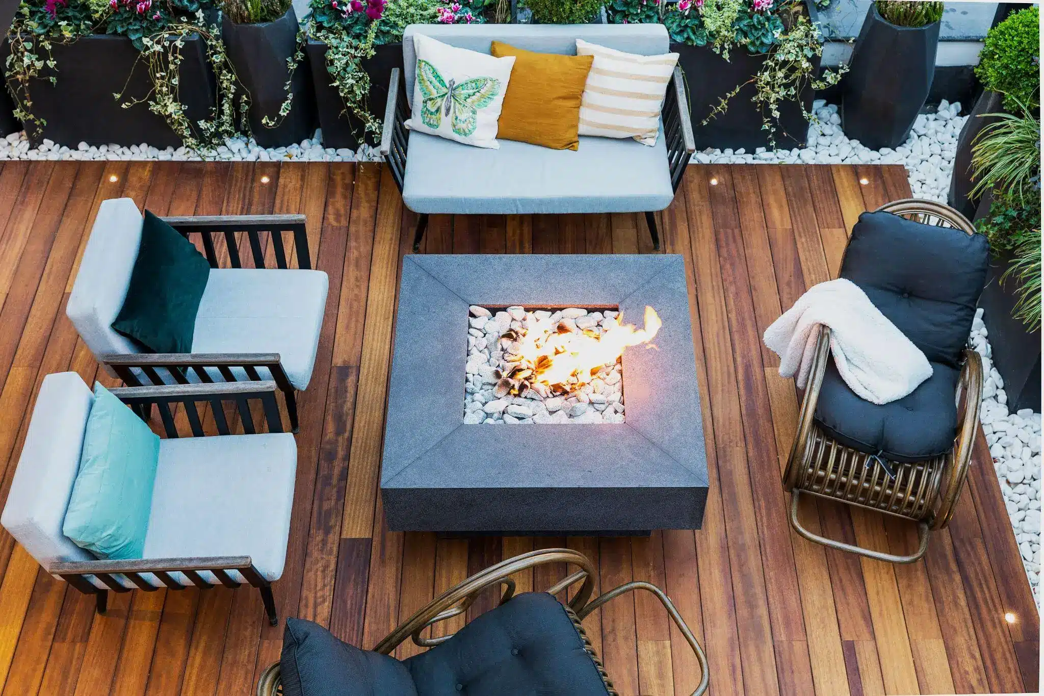 Outdoor patio with modern furniture around a lit fire pit on wooden deck