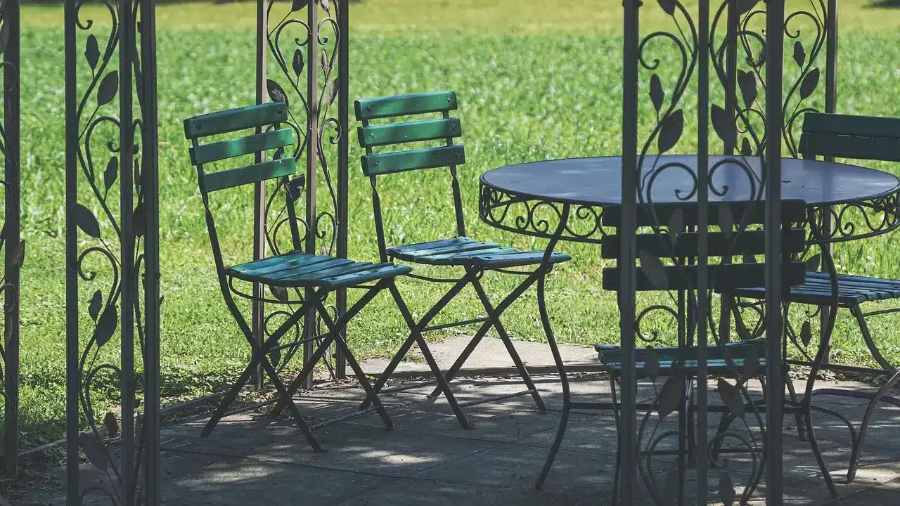 Metal patio chairs and table under decorative gazebo in sunny garden setting