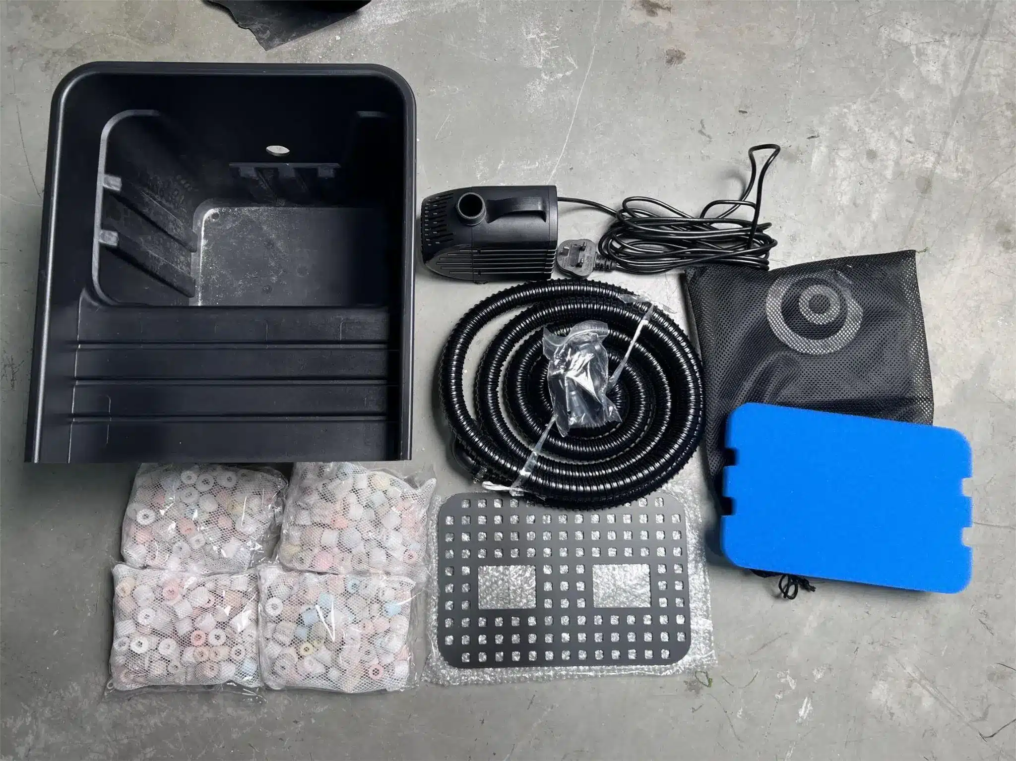 Aquarium filter kit with pump, hose, ceramic media bags, and blue sponge laid on gray floor