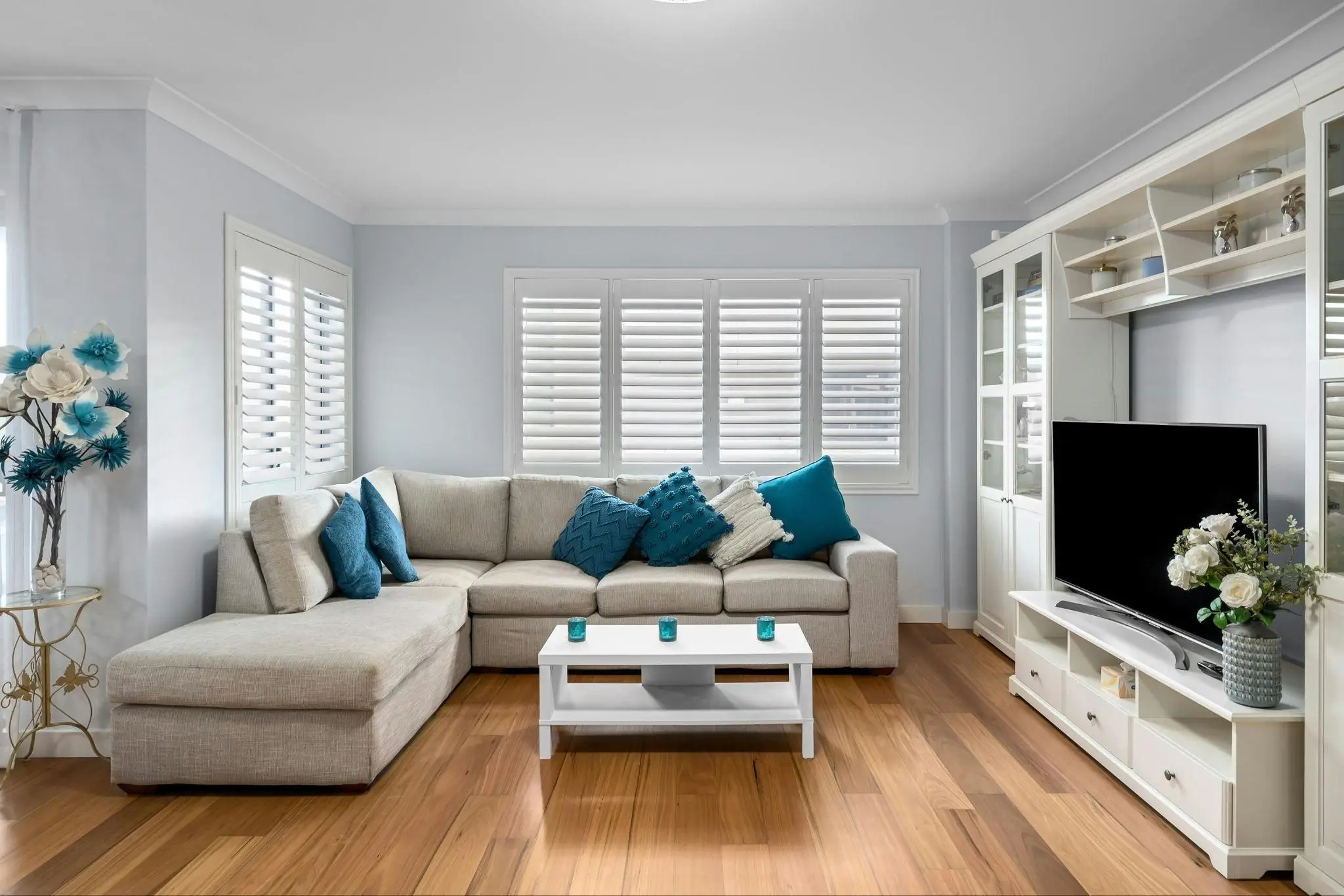 Modern living room with beige sectional sofa, teal cushions, white coffee table, and entertainment unit