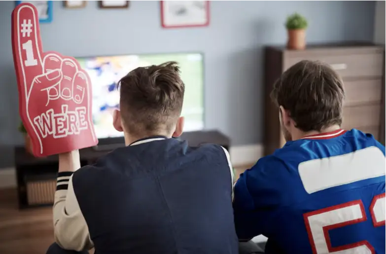 Two men watching football on TV with foam finger in living room