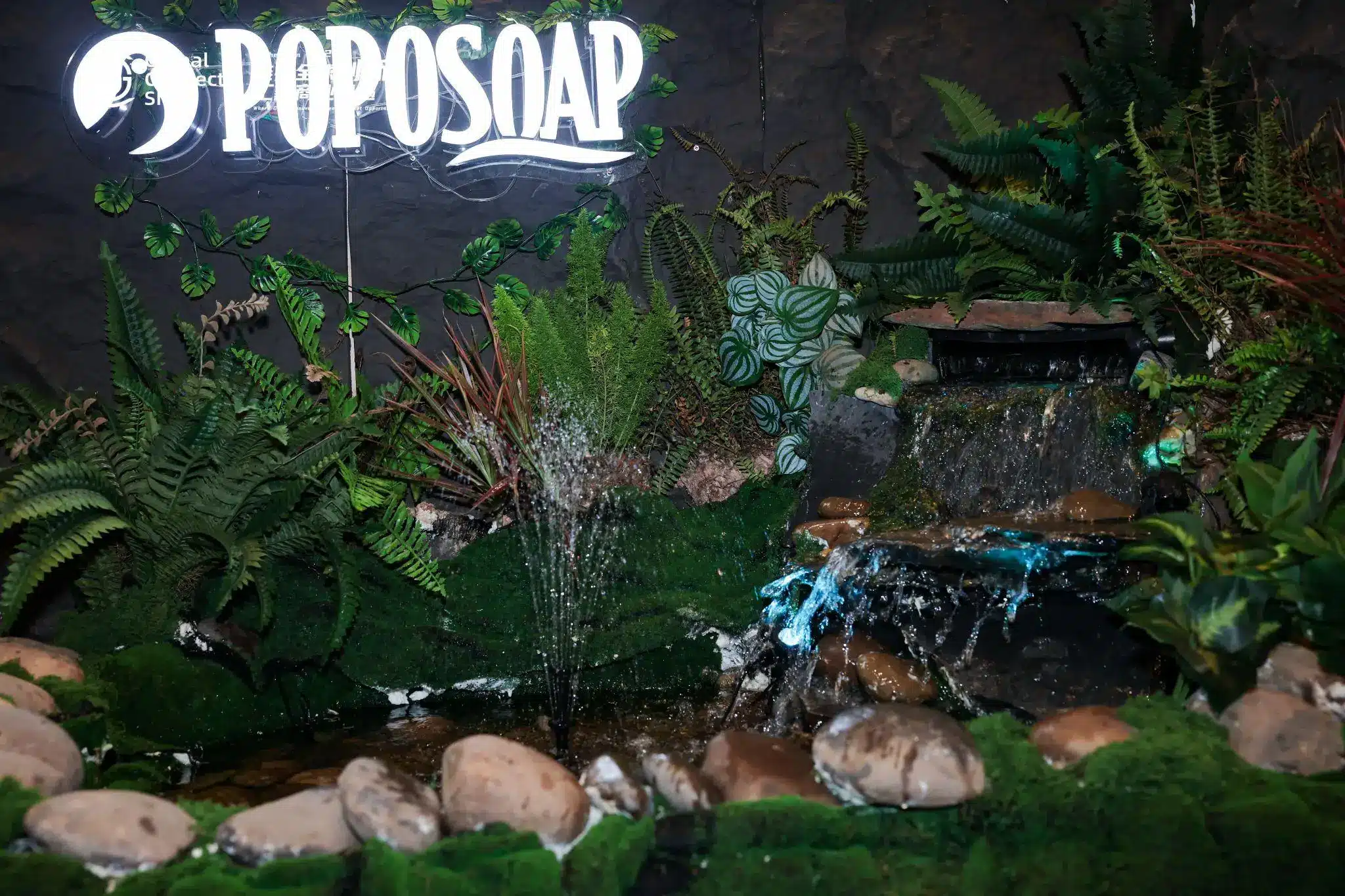 Indoor waterfall with flowing water surrounded by lush green ferns and stones