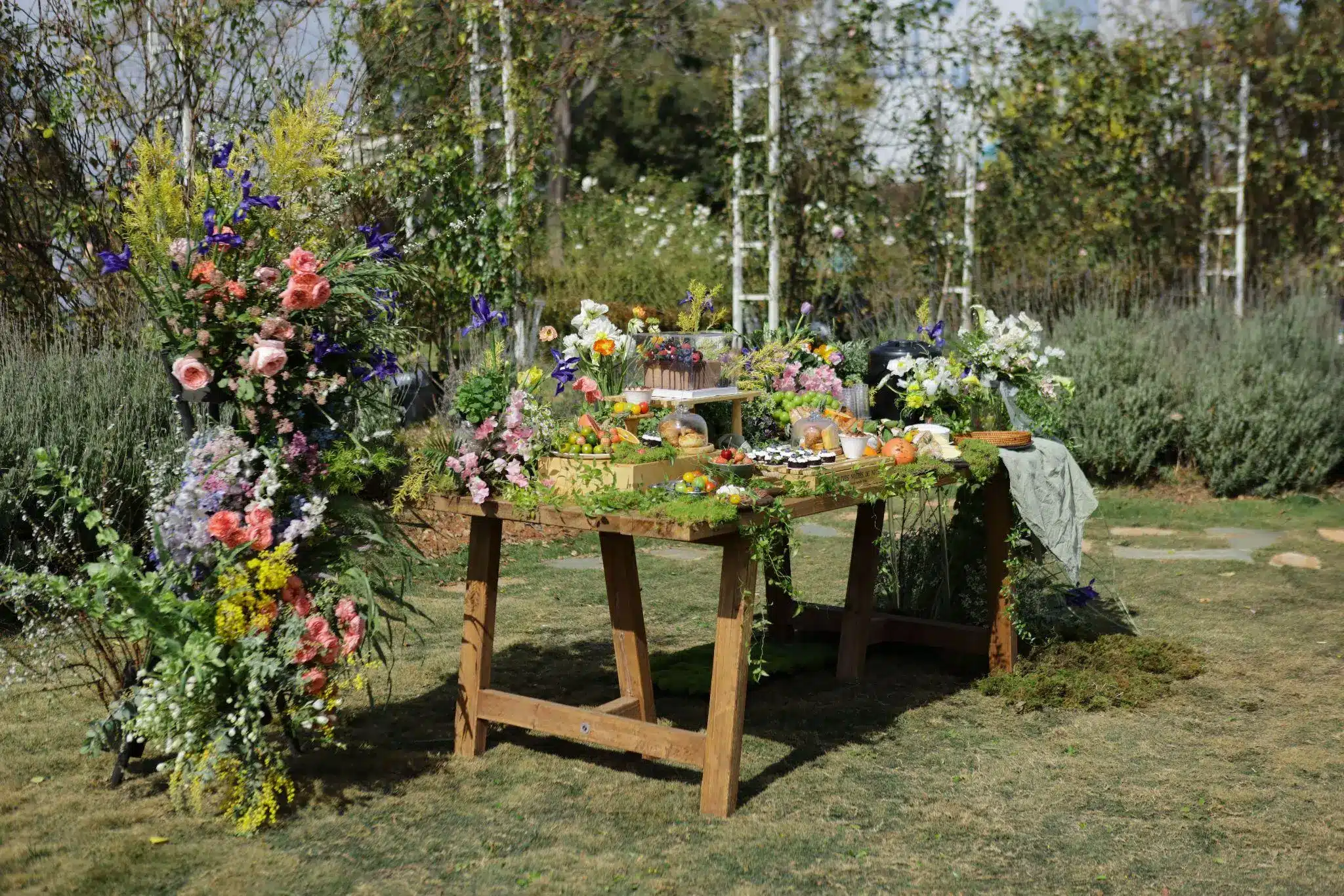 Rustic outdoor table with colorful flowers and an assortment of fresh fruits and pastries
