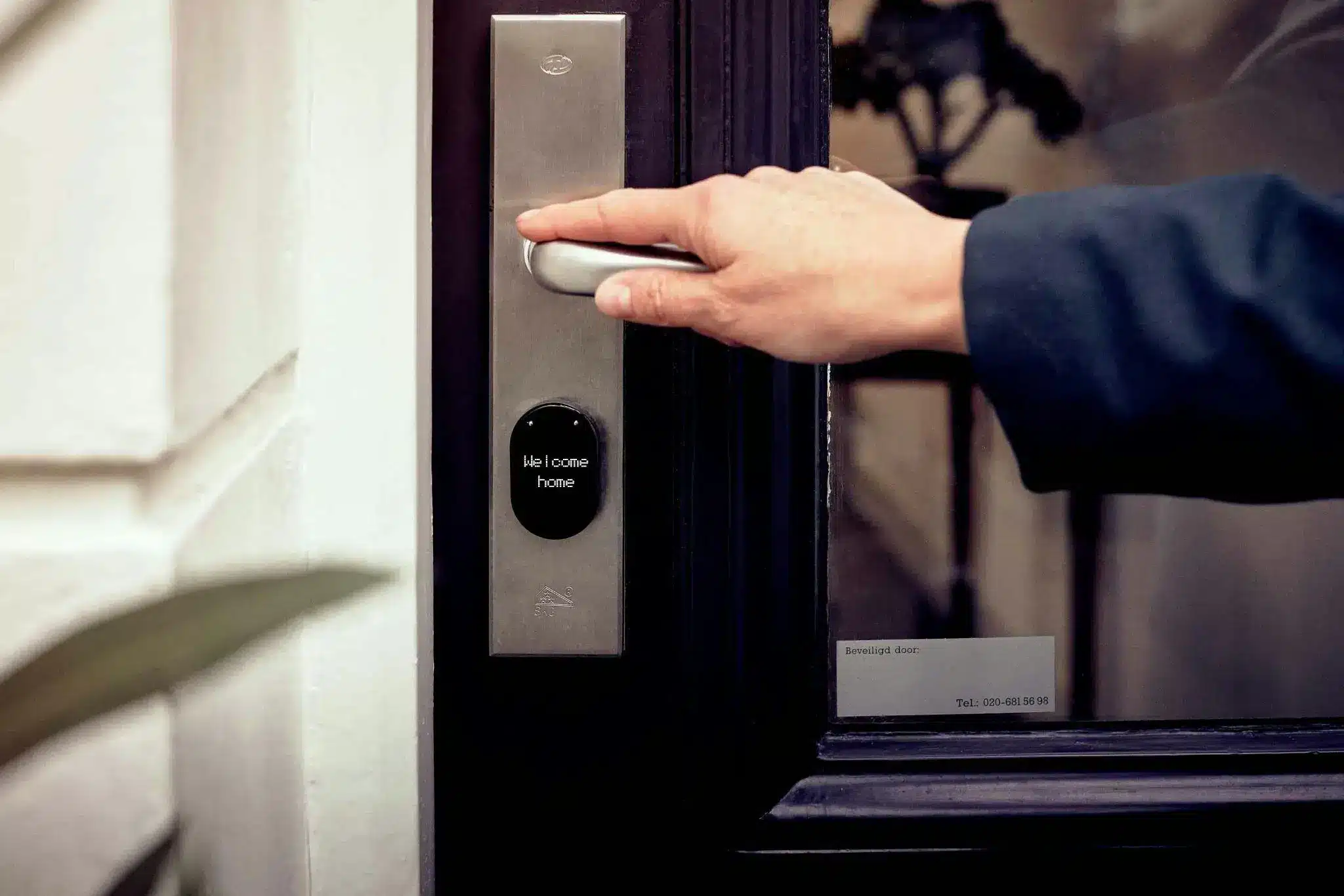 Hand pressing smart door handle with welcome message on digital display indoors