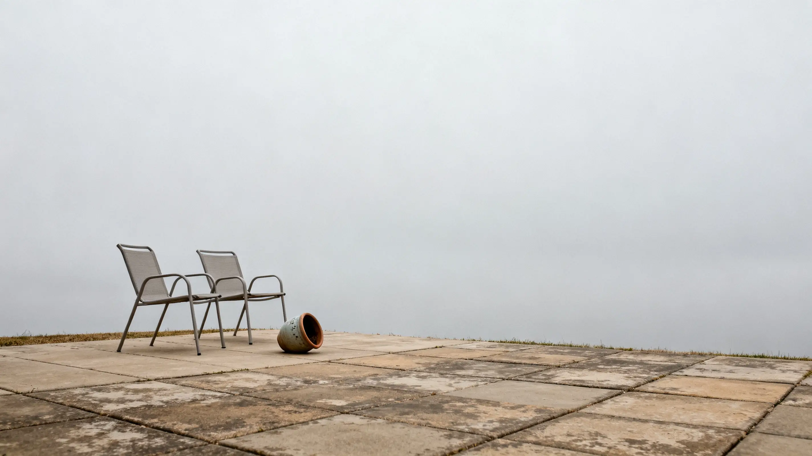 Two metal chairs and tipped over ceramic pot on foggy patio tiles