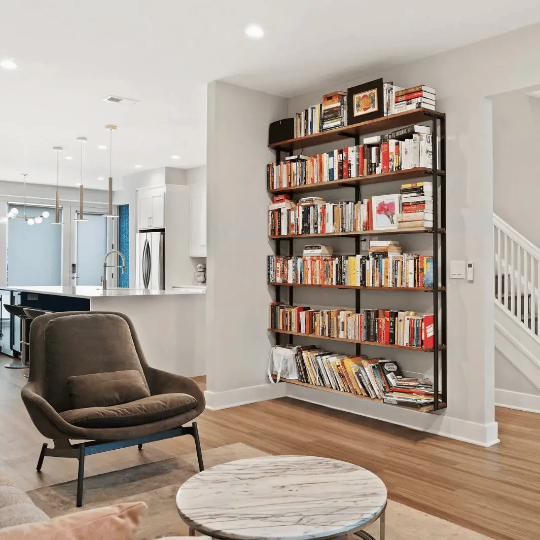 Modern living room with tall bookshelf, cozy armchair, and marble coffee table in open-concept space