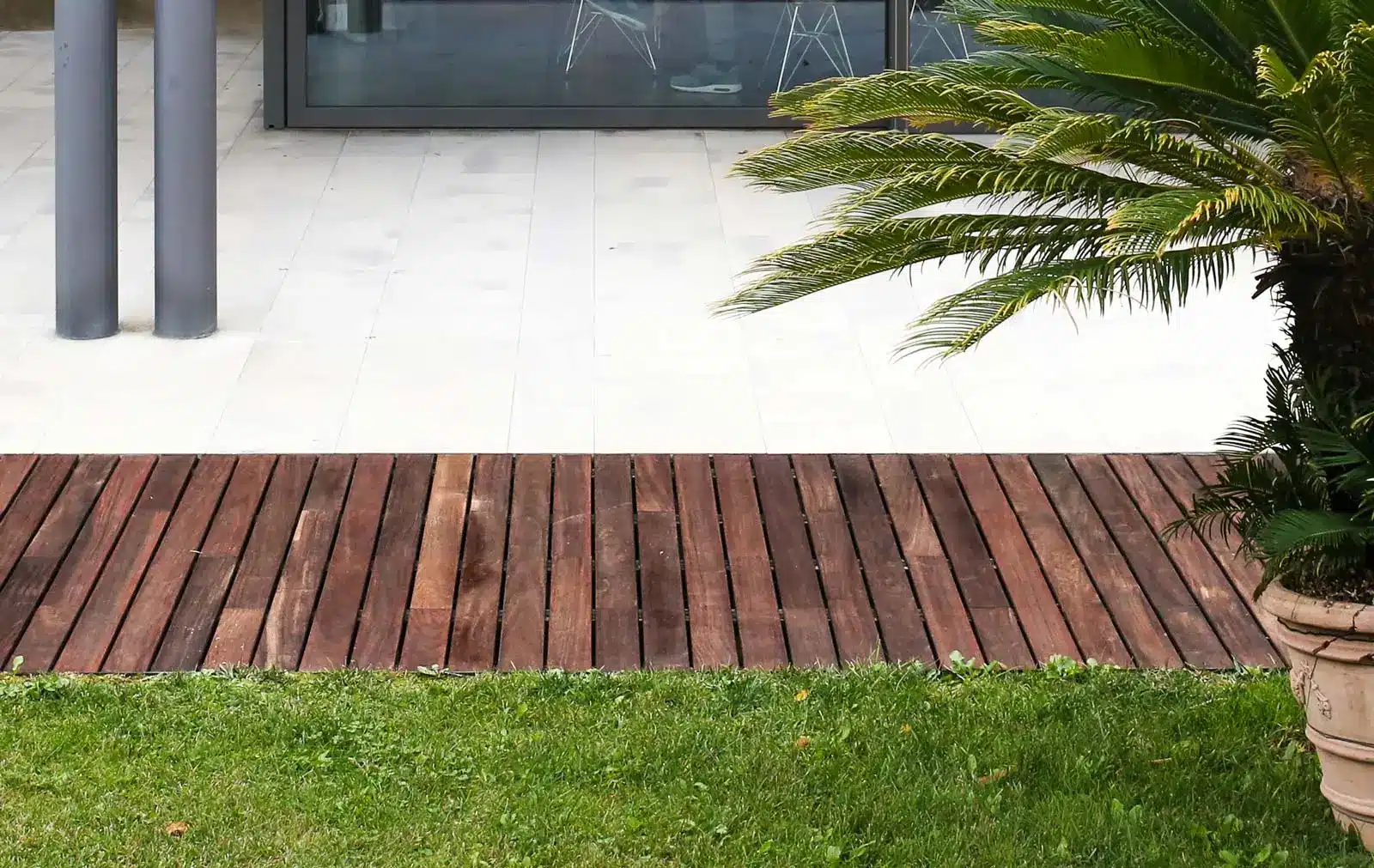Wooden deck and green lawn with potted palm near modern glass building entrance