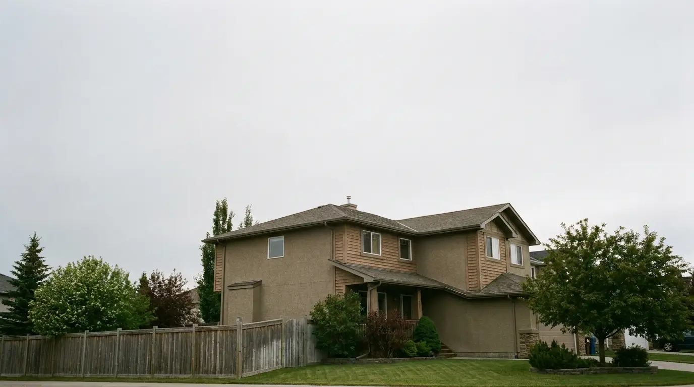 Two-story suburban house with beige siding and wooden fence in overcast daylight
