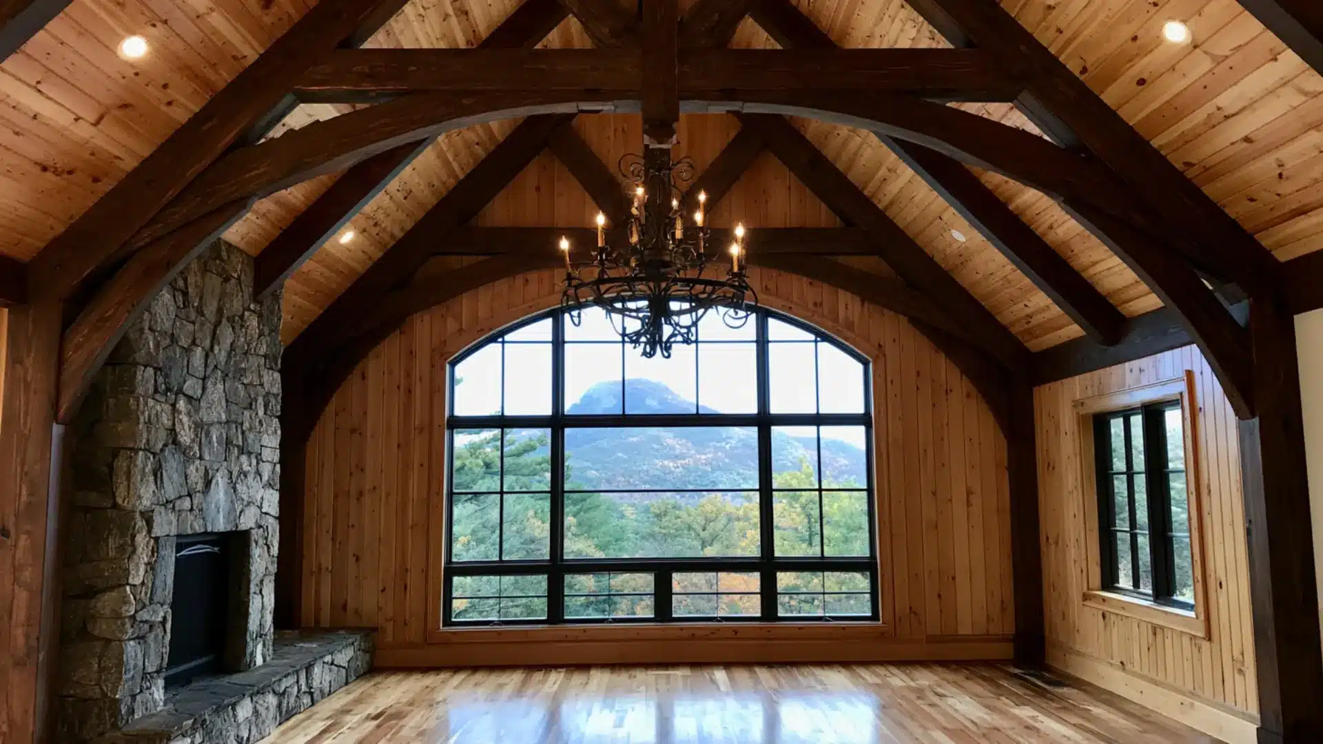 cathedral vault ceiling with dark wood trusses, stone fireplace and an arched mountain view window