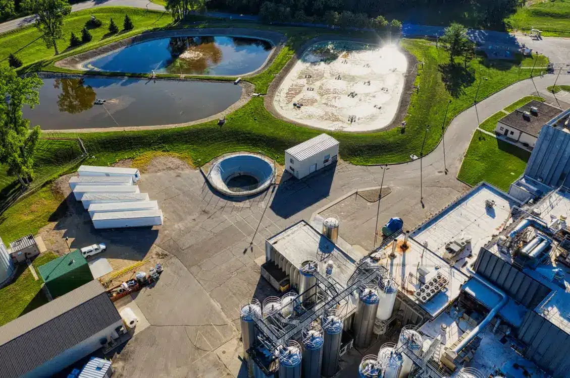 Industrial facility with storage tanks and ponds surrounded by green landscape under bright sunlight