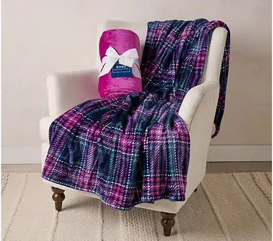 Plaid fleece throw draped over a beige armchair with a matching rolled blanket nearby