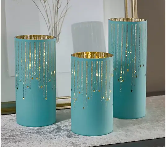 Three turquoise candle holders with gold star pattern on grey textured surface