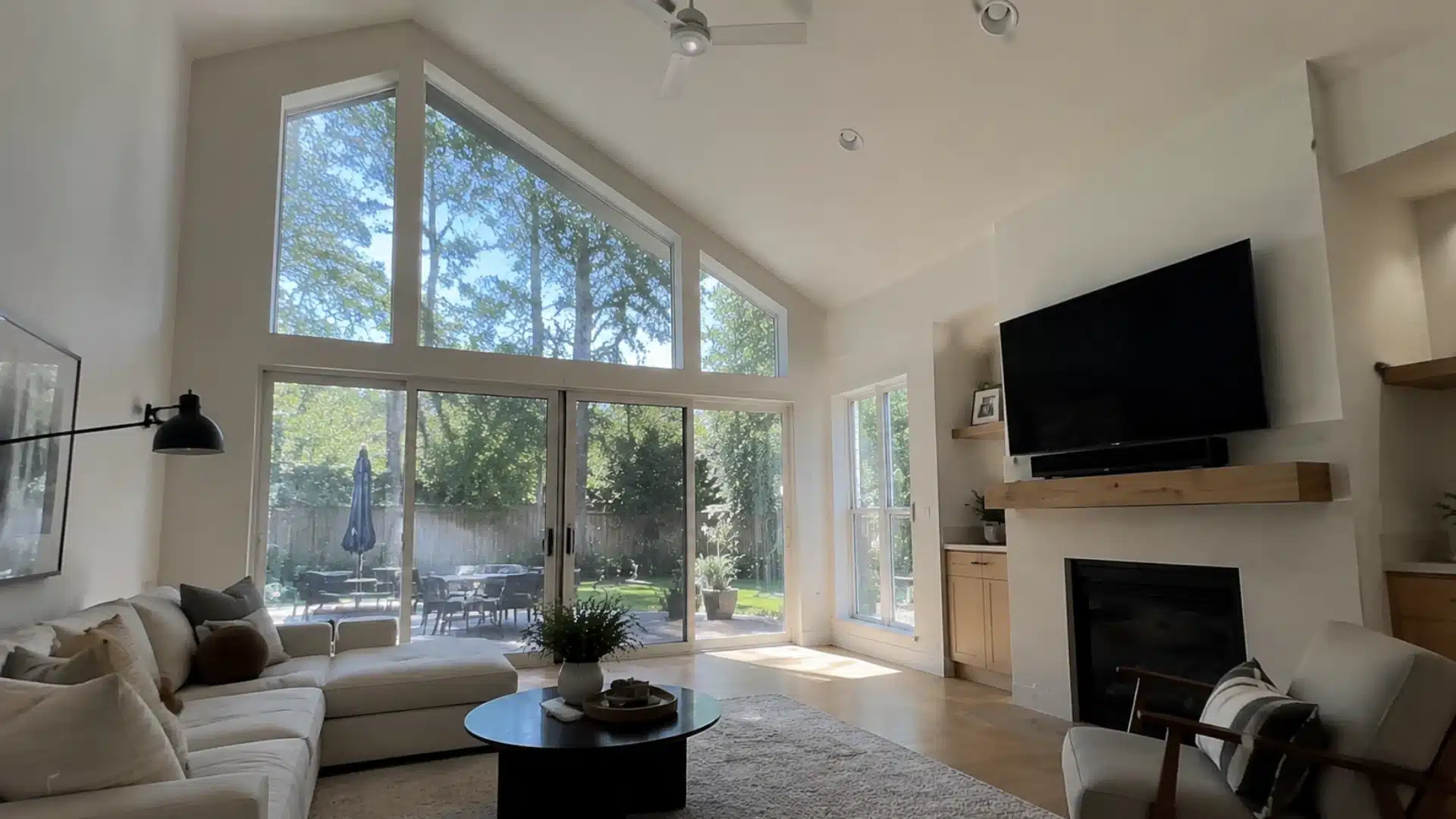 bright vaulted living room with floor to ceiling windows overlooking a wooded backyard view