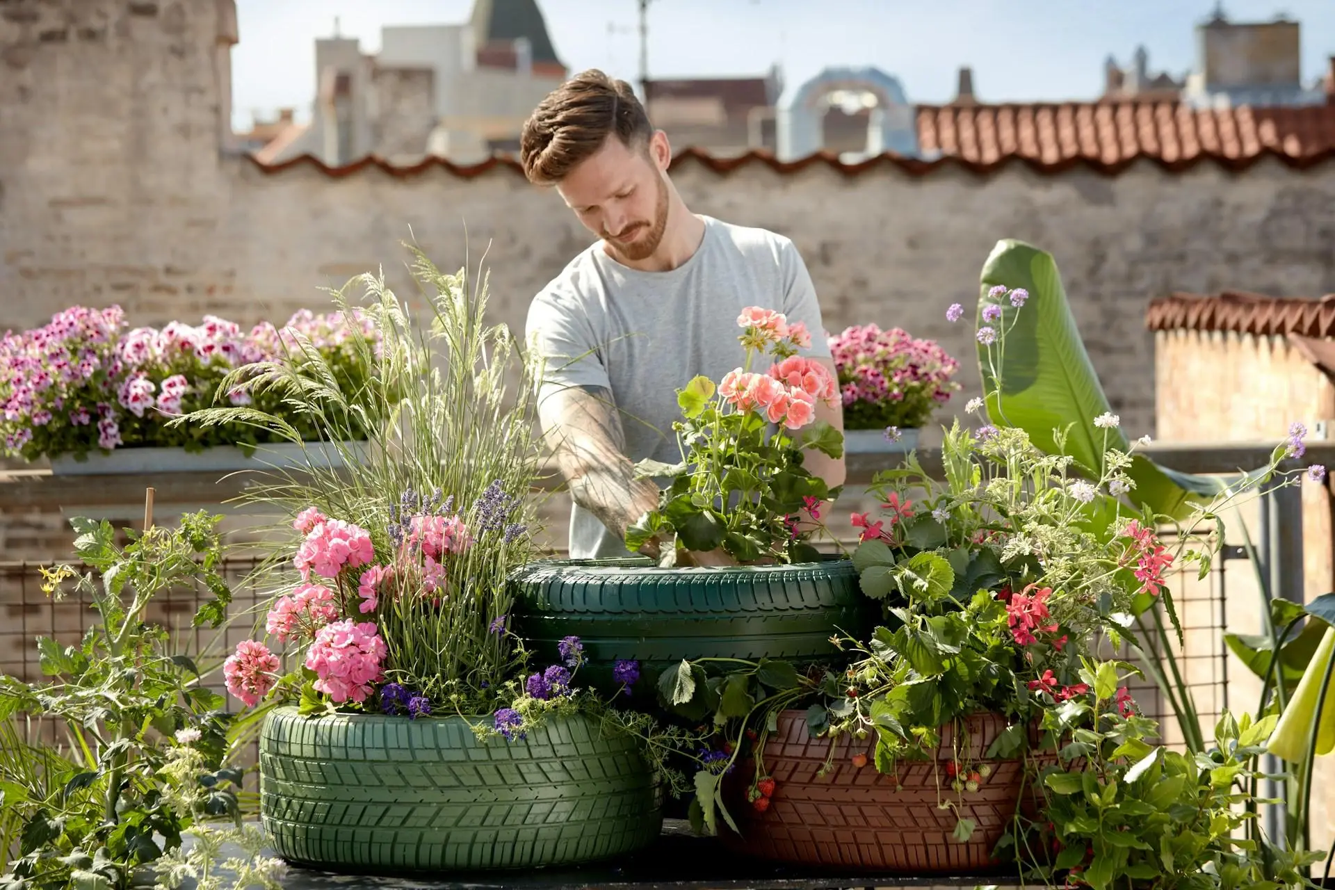 Man tending to colorful flowers in repurposed tire planters on urban rooftop garden