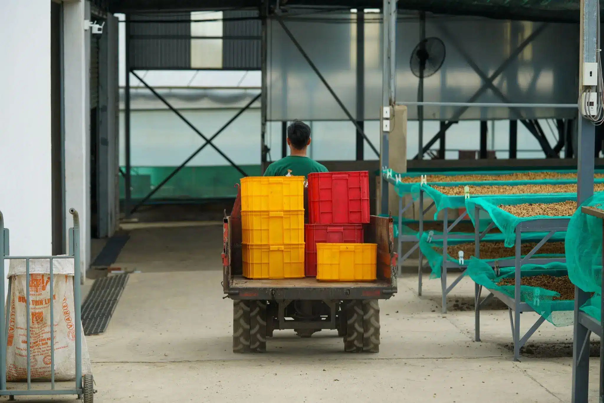 Worker driving cart with yellow and red crates in industrial warehouse setting