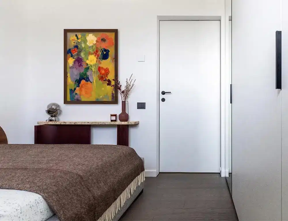 Cozy bedroom with abstract floral painting above wooden console table and textured brown bedspread