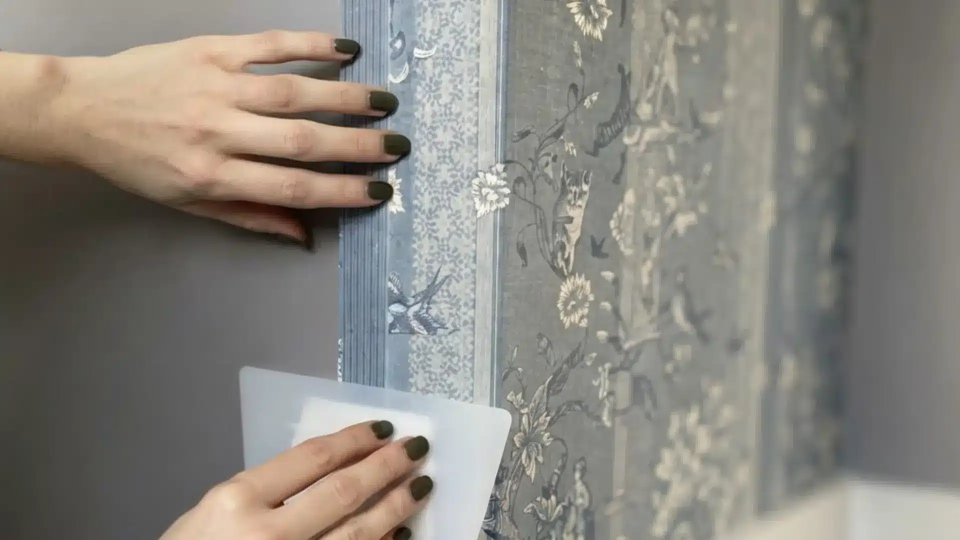 a person holding wallpaper edge in place while smoothing it flat around an outside corner