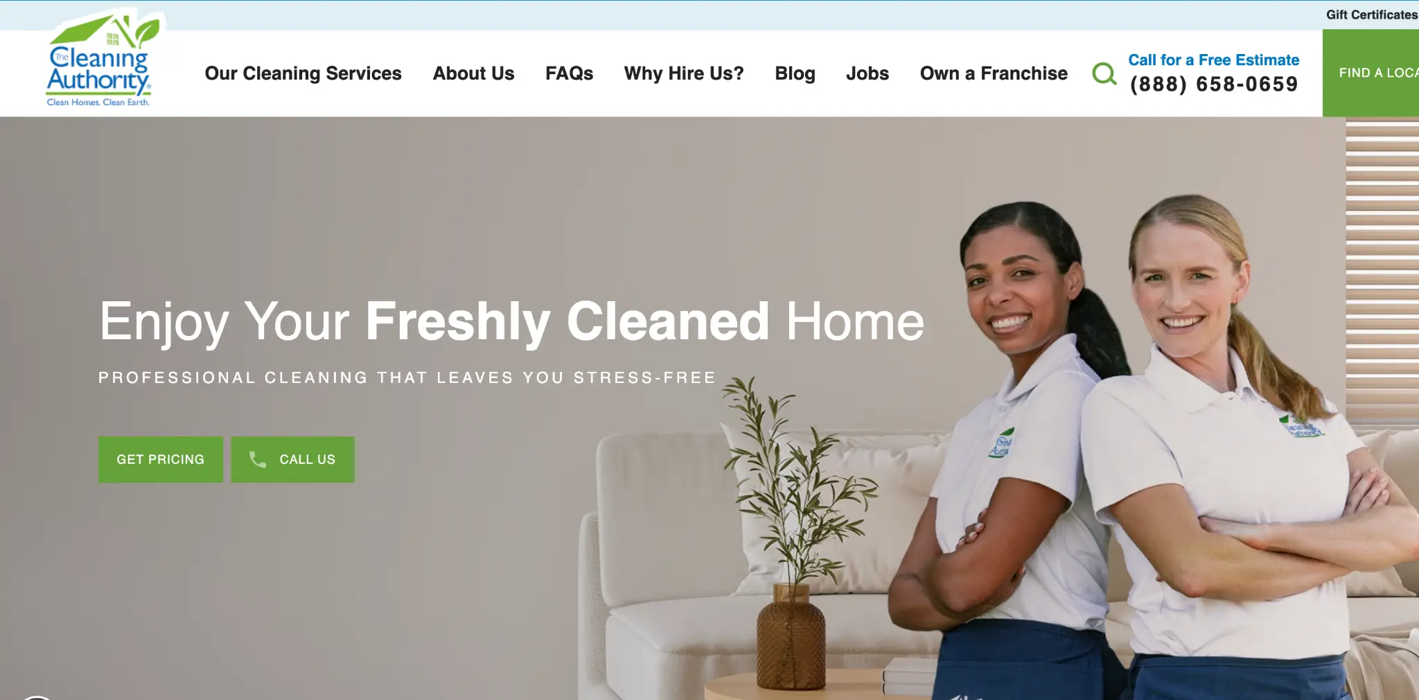 Two smiling women in white polo shirts standing indoors next to a cream sofa and potted plant
