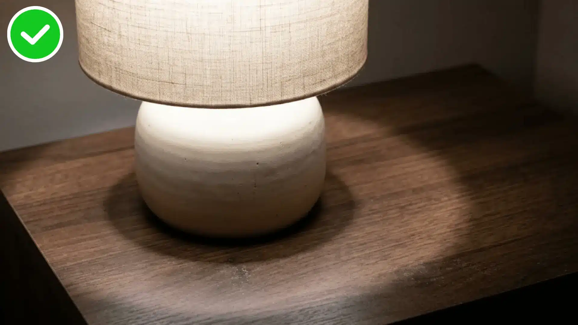 close up of a bedside lamp casting a small pool of neutral light on a nightstand