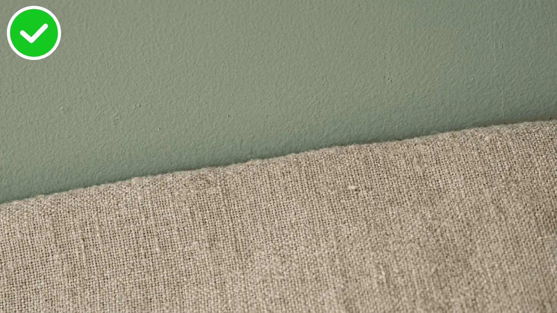close up of a sage green wall meeting a neutral linen bedspread texture
