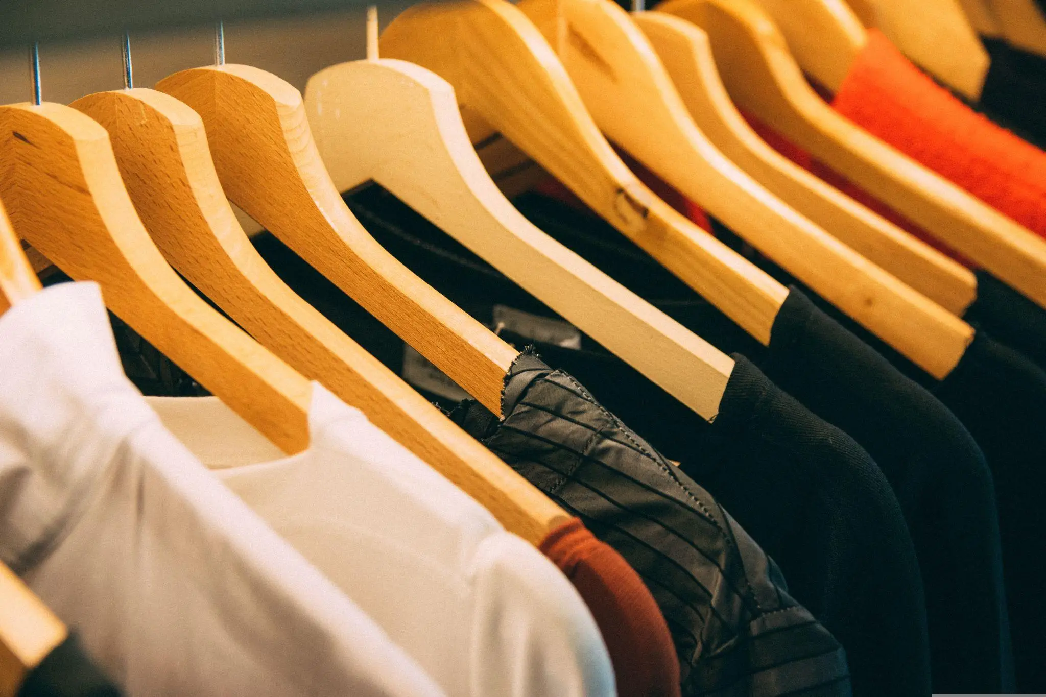 Clothing on wooden hangers in a wardrobe setting with warm lighting