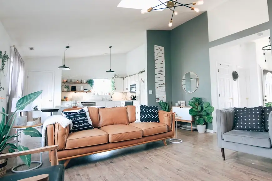 Contemporary living room with tan leather sofa, gray armchair, and kitchen in background