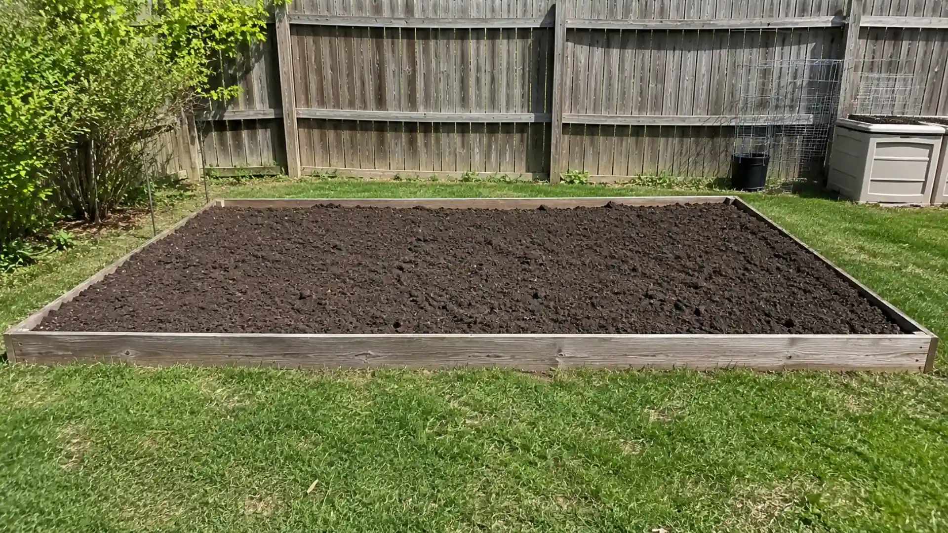 empty raised garden bed with fresh soil in an open sunny backyard ready for planting