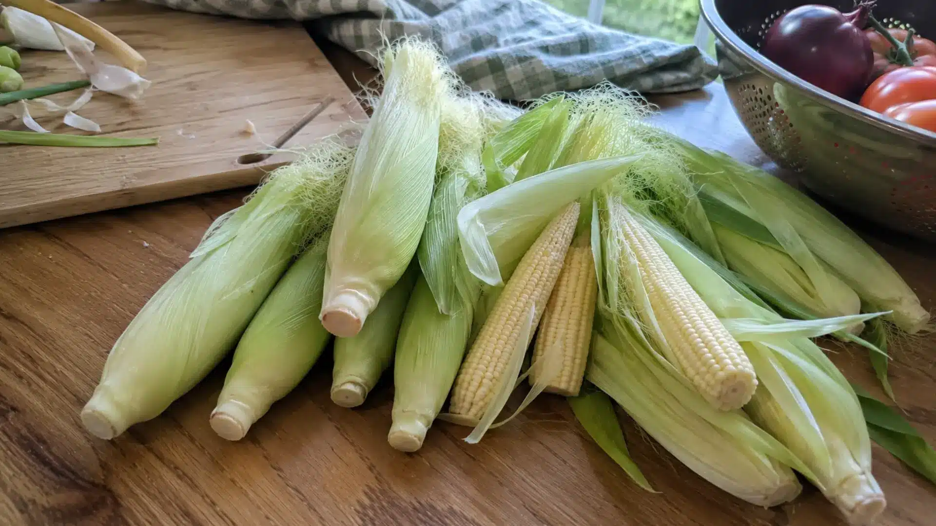 freshly harvested baby corn with peeled husks and sliced pieces on a wooden cutting board