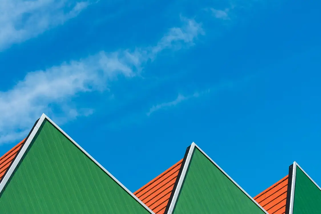 Green and red gable rooftops against a bright blue sky with wispy clouds