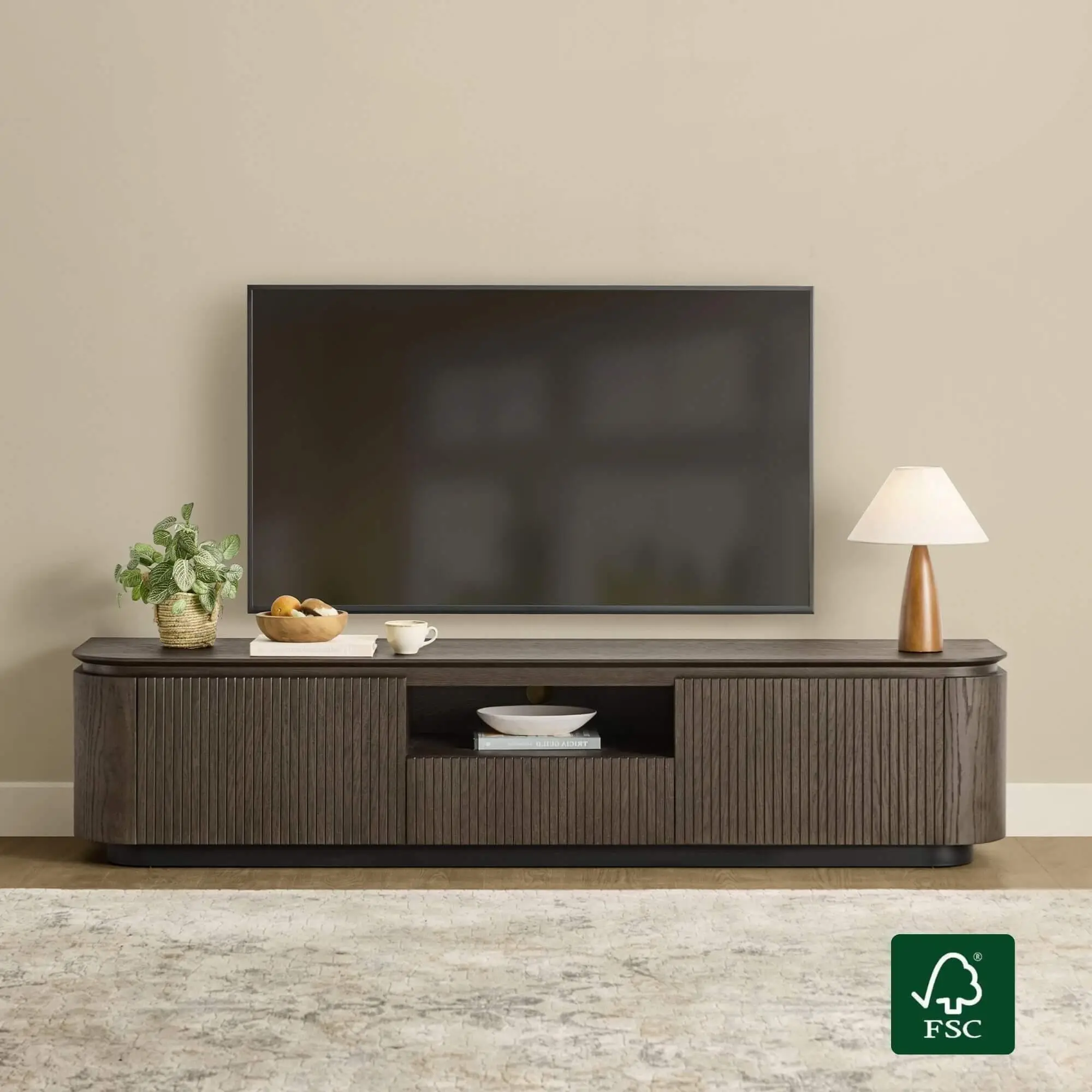 Dark wooden media console with potted plant and lamp beneath wall-mounted TV in neutral living room