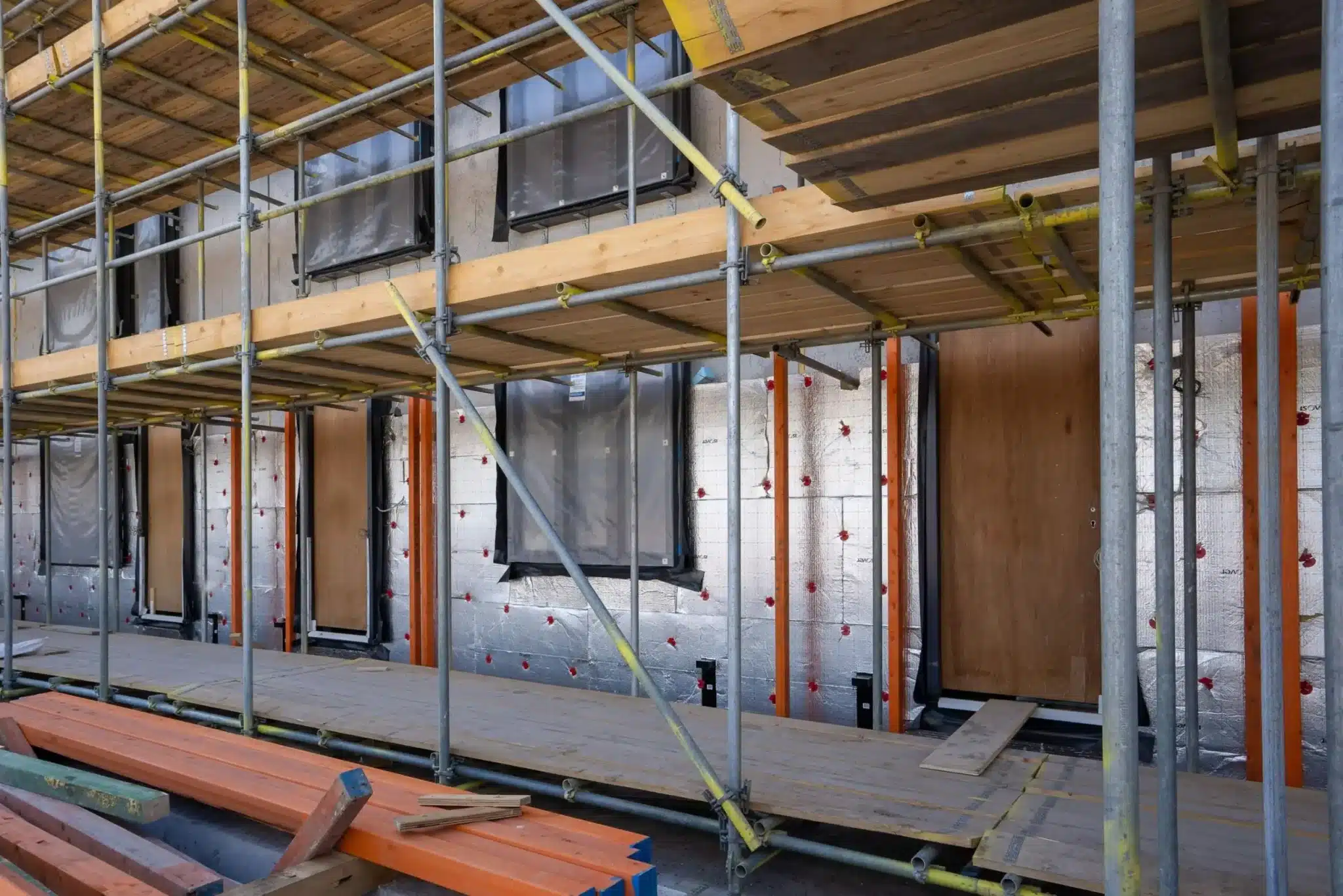 Scaffolding framework around a building under construction with exposed insulation and wooden planks