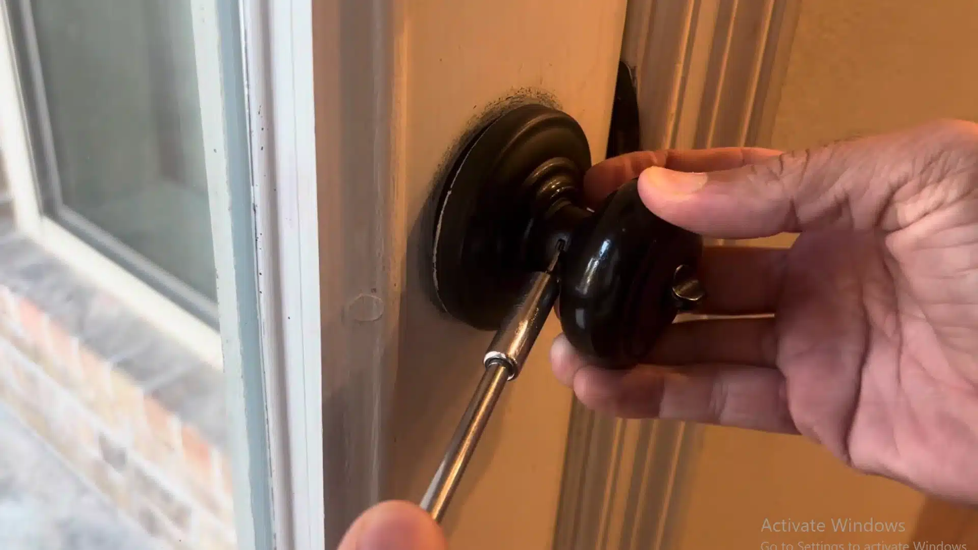 man pressing the small release tab on a black door knob using a flathead screwdriver