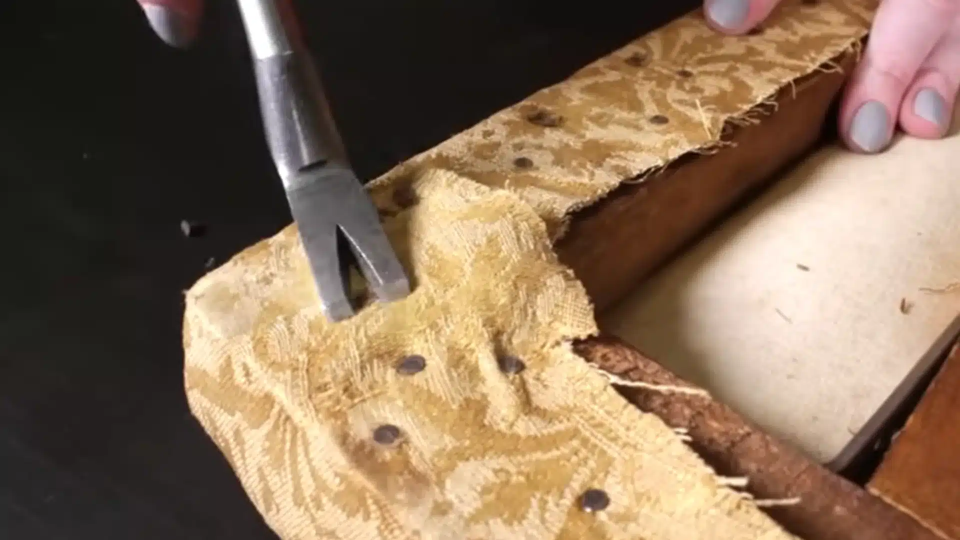 old upholstery fabric and staples being removed from a wooden chair seat using an upholstery tool