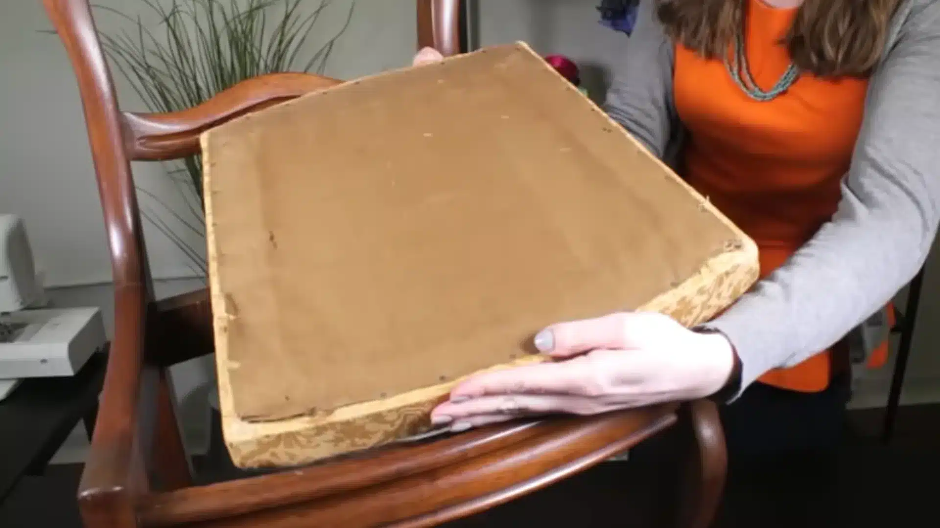 person removing a worn seat cushion from a wooden dining chair before beginning the reupholstery