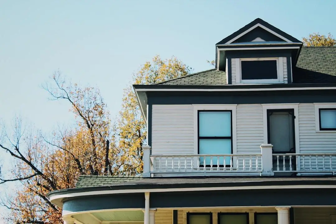 Second story of a vintage house with blue trim and frosted windows against autumn trees