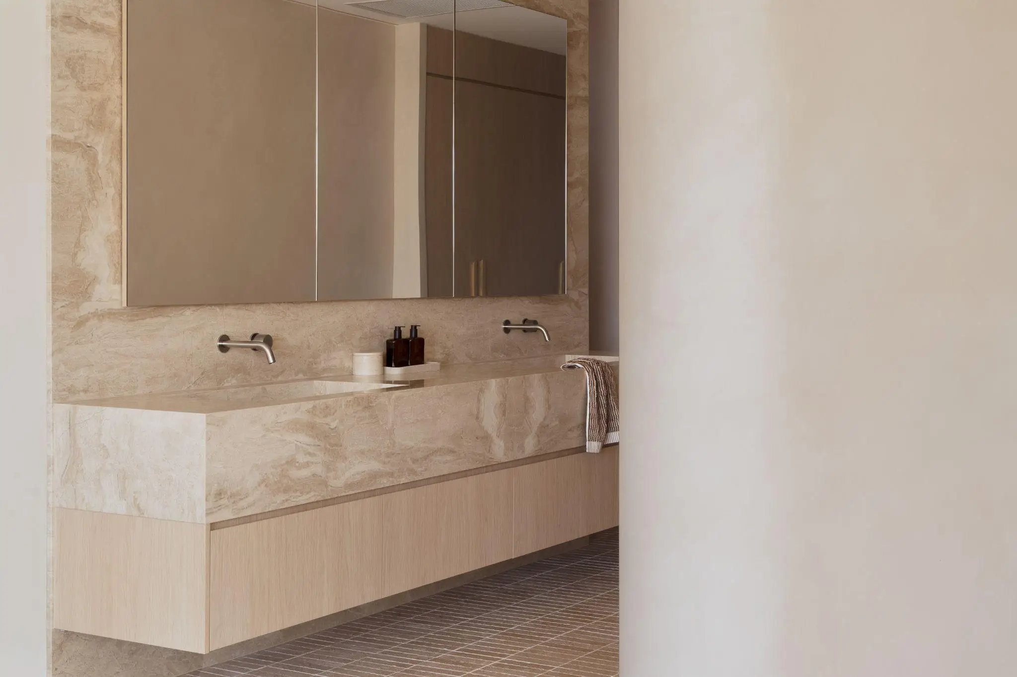 Minimalist bathroom with marble countertop and mirror, featuring chrome faucets and neutral tones