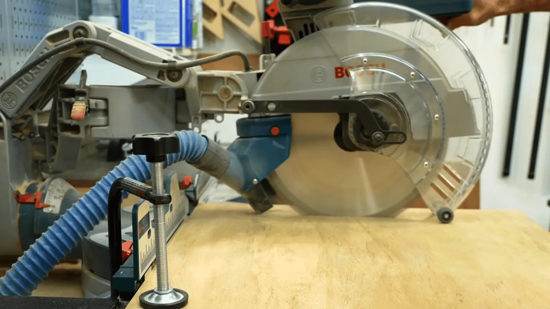 sliding miter saw with dust hose attached, positioned above a plywood workpiece with a stop block clamp