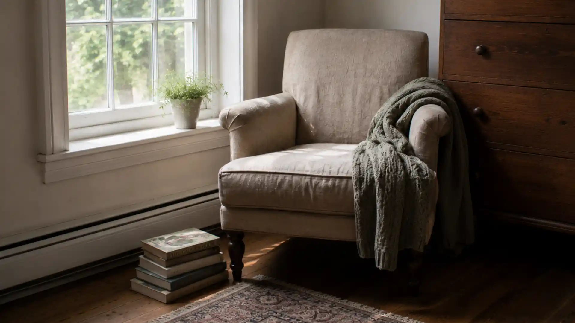 small armchair reading nook with knit throw and stacked books by window